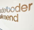 A white wall with large, three-dimensional metallic letters spelling out "adelboode" and "almennd" in a modern, sleek design.