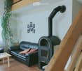 Living room with a black leather sofa, small wooden table, and a black wood-burning stove. The room has tiled flooring and a wooden staircase leading to an upper level.