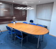 oval conference table, blue chairs, wooden floor, white walls, windows, whiteboard