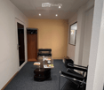 Empty room with carpeted floor, glass table, modern chairs, cabinet with clothes hanging, trash can, door on the right, window, mirror