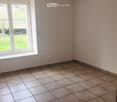 Empty room with tiled floor and white walls, featuring a large window with white frame and a view of a green outdoor area.