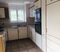 Modern kitchen with white cabinets, tiled walls, and a window overlooking a green field. Features include a sink, dishwasher, and oven.