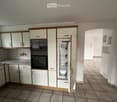 A modern kitchen with white cabinets, a stainless steel oven, a refrigerator, and a sink, featuring tiled walls and floors.