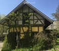 Traditional timber-framed house, yellow walls, red roof, surrounded by greenery