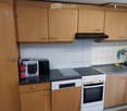 Modern kitchen with wooden cabinets, white tiles, and stainless steel appliances including an oven, fridge, and sink.