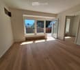 Empty room with wooden flooring, large windows, and a sliding glass door leading to an outdoor area.