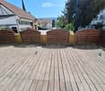 Wooden deck with a wooden fence, surrounded by residential buildings and trees.