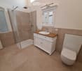Modern bathroom with a white cabinet, wooden countertop, sink, faucet, toilet, and a glass-enclosed shower with a handheld showerhead.