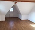 Empty attic room with wooden flooring, white walls, and a skylight window. No furniture or equipment present.