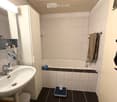 Modern bathroom with white tiles, a sink with a mirror cabinet, a bathtub, a towel on a rack, and a scale on the floor.