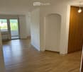 Empty hallway with wooden flooring, white walls, and a door leading to a balcony area.