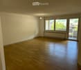 Empty room with wooden flooring, white walls, large windows, and a sliding glass door leading to a balcony.