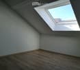 Empty attic room with wooden flooring, white walls, and a skylight window allowing natural light.