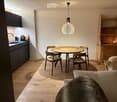 Open-plan living and dining area with modern furniture, including a sofa, coffee table, dining table with chairs, kitchen cabinets, and a pendant light.