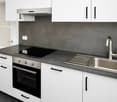 Modern kitchen with white cabinets, stainless steel sink, oven, and range hood. Dark countertops and backsplash.