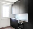 Modern kitchen with dark cabinets, a stainless steel oven, a sink with a faucet, and a window letting in natural light.