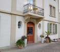 Classic European building with a balcony, ornate wrought-iron railing, and potted plants near the entrance.