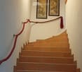 Spiral staircase with wooden handrails and tiled steps, framed artwork on the wall, and a red rope barrier.