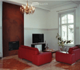 Modern living room with red leather sofas, a coffee table, a television on a stand, a chandelier, a fireplace, and a potted plant near the window.