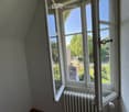 Empty room with wooden flooring, white radiator, and large windows offering a view of a garden and trees.