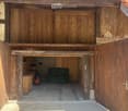 Wooden garage with large double doors, interior contains a green sofa and a red gas cylinder.