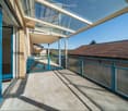 Balcony / Terrace. Spacious balcony with a modern glass roof and blue railings, overlooking a residential area with a clear blue sky.