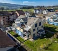 House. Aerial view of a residential area with multiple houses, surrounded by green fields and distant hills.