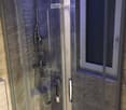 Modern glass-enclosed shower with a rainfall showerhead and handheld sprayer, marble walls, and a sleek chrome frame.