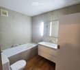 Modern bathroom with a bathtub, toilet, sink, and mirror. Light grey tiles and wooden flooring.