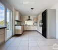 Modern kitchen with light wooden cabinets, stainless steel appliances, and tiled flooring.