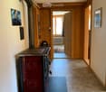 A hallway with wooden paneling, a red wood-burning stove, and a blue mat. The hallway leads to another room with a visible rug and radiator.