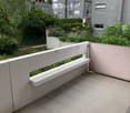 Balcony with tiled floor, white railing, overlooking a landscaped garden area with trees and shrubs.