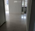 Empty hallway with light-colored walls and a polished concrete floor, leading to an adjacent room with white cabinets and a window.