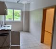 Empty kitchen with tiled floor, white walls, and a window overlooking a green area. Basic cabinetry and sink are present, but no appliances or furniture.
