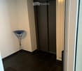 Hallway with dark tiled floor, white walls, elevator, small decorative table, and trash bin.