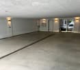 Empty underground garage with concrete floor, white walls, and a large garage door on the left side.
