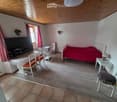 Furnished Room. Cozy bedroom with a bed, table, chairs, microwave, and a large screen. The room features wooden flooring and a slanted wooden ceiling.
