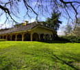 A large, two-story yellow house with a brown tiled roof, surrounded by a well-maintained green lawn and trees.
