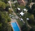 Aerial view of a large outdoor area with a swimming pool, several tents, and scattered chairs and tables, surrounded by trees and pathways.