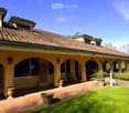 Two-story house with a tiled roof, arched covered walkway, and well-maintained garden with potted plants and a lawn.