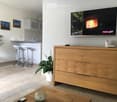 Open kitchen area with two stools, potted plants, wooden cabinet, tile floor, television, counter with cabinets