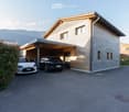 Modern two-story house with a covered garage, two parked cars, and a view of mountains in the background.