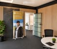 Modern office space with a round table, office chair, potted plant, and a large screen displaying a promotional image.