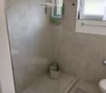 Modern bathroom with a glass-enclosed shower, toilet, and a small storage basket inside the shower. A grey bathroom rug is placed next to the toilet.