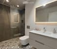 Modern bathroom with a white sink, chrome faucet, large mirror with built-in lighting, toilet, glass-enclosed shower, and decorative patterned tiles.