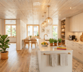 Bright, modern kitchen with white cabinets, marble countertops, and wooden flooring. Features a central island with a sink, pendant lights, and a dining area with a table and chairs. Includes various appliances, potted plants, and decorative items.