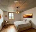 Cozy bedroom with wooden bed, desk, chair, and large window overlooking a scenic landscape.