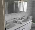 Modern bathroom with double sink vanity, large mirror, and toilet. Grey tiles and white cabinetry.