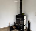 Corner room with a modern black wood-burning stove, storage compartments, and wood logs nearby.