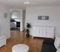 Modern living room with a black sofa, white coffee table, white cabinet, potted plant, flat-screen TV, wall clock, and picture frame.